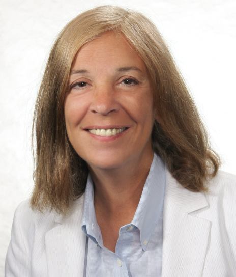 Shoulder-high portrait of woman in her fifties with shouder-length hair wearing a white suitcoat and light blue shirt.