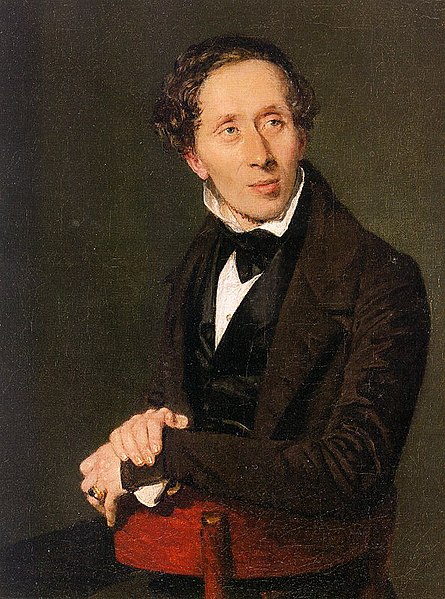 Waist high portrait of young man facing right center with folded hands, wearing a suit and floppy bow tie